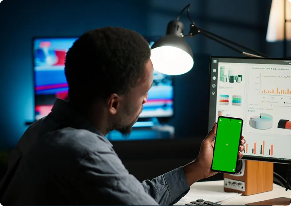 Developer testing a mobile app on a phone beside a desktop monitor