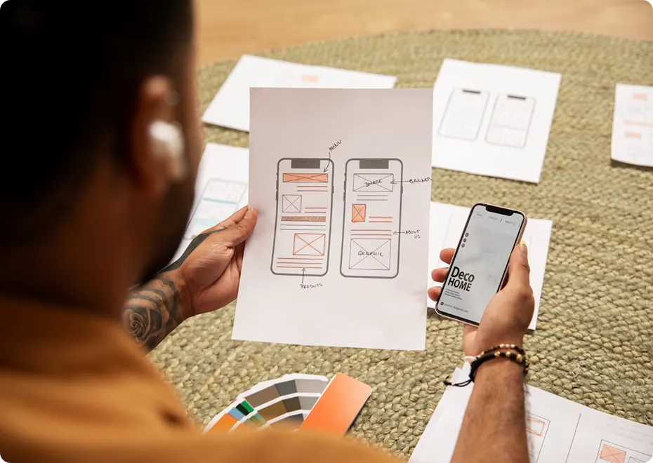 Designer comparing printed app wireframes with a phone screen