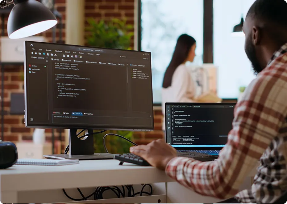 Developer writing code on a dual-monitor workstation in a bright office